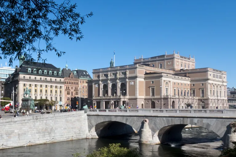 Stora byggnader mot en blå himmel, i förgrunden ett vattendrag.