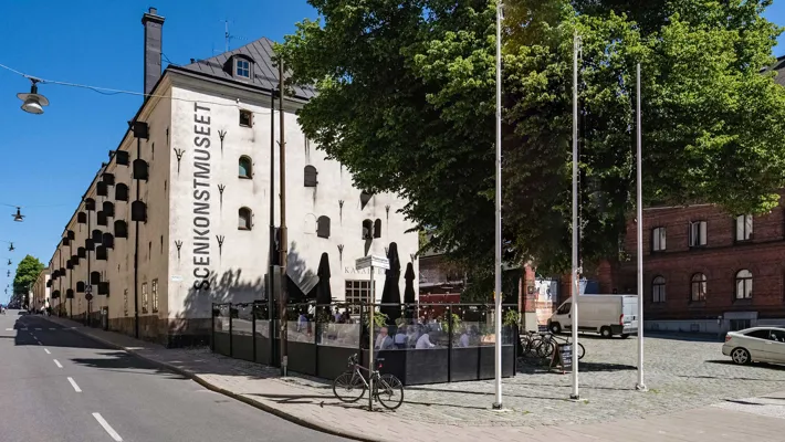 En vit byggnad med många fönsterluckor och stort träd framför.