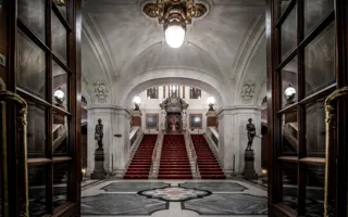 Utsikt över en stor entréhall, en trappa med röd matta leder uppåt mot en dörr.