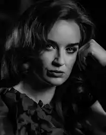 A close-up of a woman's face, she leans her head against her left hand.