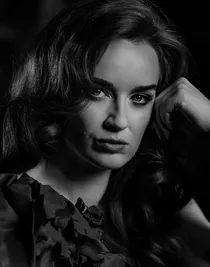 A close-up of a woman's face, she leans her head against her left hand.