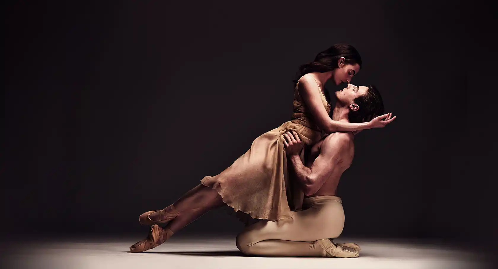 Two ballet dancers in a dynamic pose on a stage with a dark background, emphasizing their movement and expression.