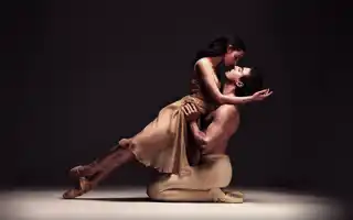 Two ballet dancers in a dynamic pose on a stage with a dark background, emphasizing their movement and expression.