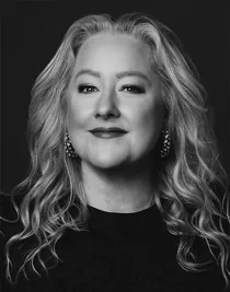 A close-up of a blonde woman wearing a dark sweater and large earrings.