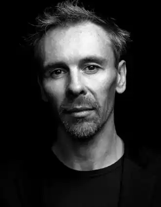 A close-up of a man with short, bushy hair and a beard.