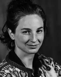 A close-up of a woman with dark hair: she is wearing a patterned knitted cardigan.