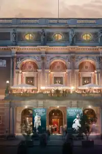 En stor fasad med träd framför som badar i sommarkvällsljus, i bakgrunden en kyrka.