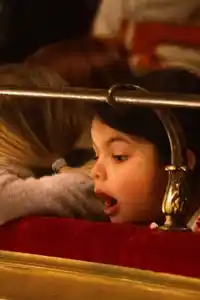 Person med blont hår vilar huvudet på kanten i en teatersalong - en andra person tittar med öppen mun mot scenen.