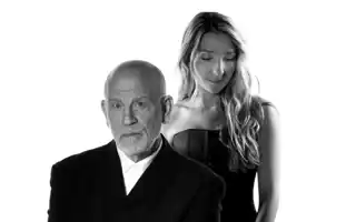 A man in a suit, behind him stands a woman with long hair.