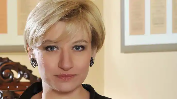 Portrait of a blonde woman against a light background, in the background a chair back.
