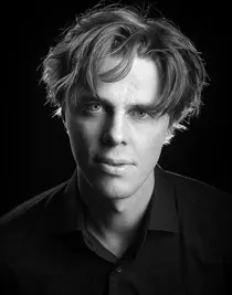 Close-up of a man with messy hair and a dark shirt.