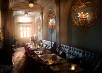 Ett mörkt rum med stolar och bord, solen lyser genom ett fönster i bakgrunden.