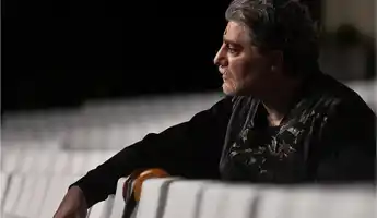 A man in profile resting his arms against the backs of chairs.