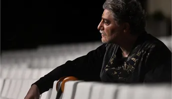 A man in profile resting his arms against the backs of chairs.