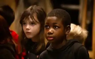 A photo of children in an indoor environment. The children wear colorful clothes and seem engaged in an activity.