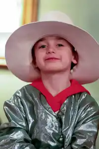 Three younger children in a row, the child in the middle has a hat and is dressed up.