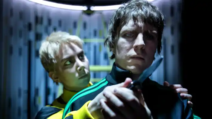 A man stands behind another man and holds a knife in front of his face.