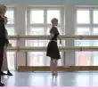Four people try out ballet at a bar in front of three windows.