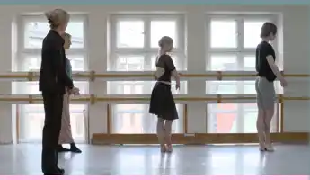 Four people try out ballet at a bar in front of three windows.