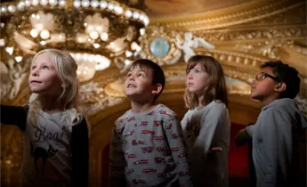 A group of young children standing in front of a chandelier.