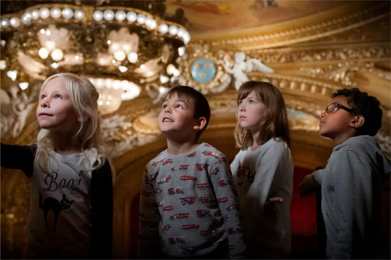 A group of young children standing in front of a chandelier.