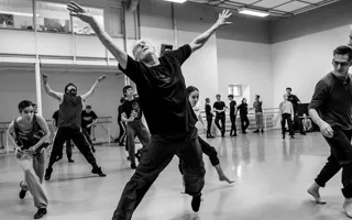 Several people in a room, some dancing, in the middle a man in motion, arms stretched up in the air.