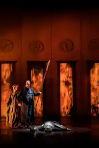 A group of people standing on a stage, fire behind them.