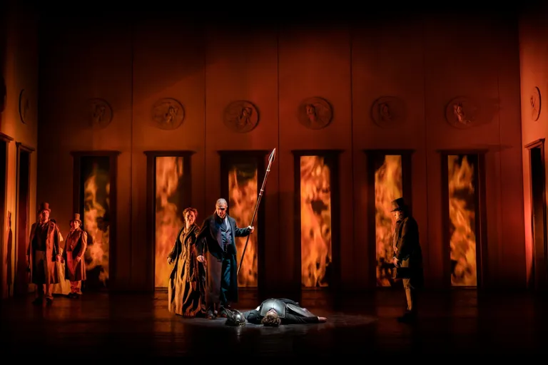 A group of people standing on a stage, fire behind them.