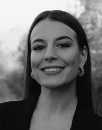 Close-up of a woman with long dark hair and earrings, wearing a dark jacket.
