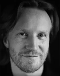 Extreme close-up of a smiling man with a beard wearing a dark shirt.