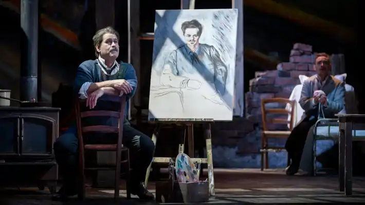 A man sits in front of a painting on an easel.