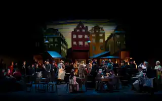 A group of people on a stage - in the background house facades.