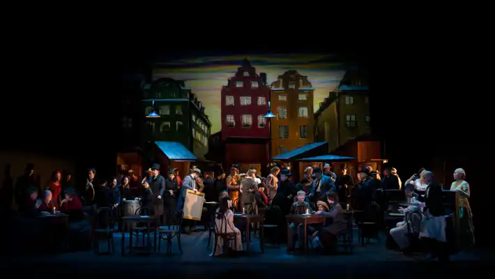 A group of people on a stage - in the background house facades.