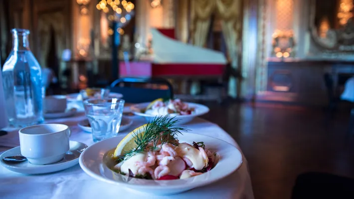 A table set with a shrimp salad, a glass of water and a coffee cup.