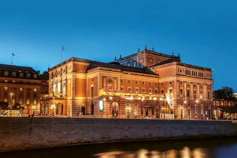 A large building by a stream against a clear evening sky.