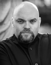 Close-up of a man with a serious expression, wearing a dark suit jacket.