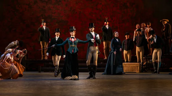A scene with many dancers, in the middle a handsome couple in riding clothes and top hats.