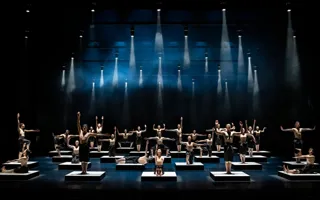 A large number of dancers are placed on cubes on the stage floor - above them spotlights.
