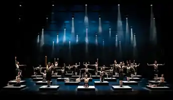 A large number of dancers are placed on cubes on the stage floor - above them spotlights.