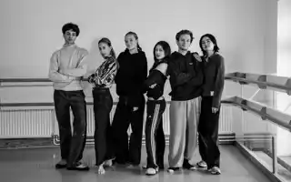 A black and white image of six young men and women standing lined up against a white wall.