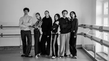 A black and white image of six young men and women standing lined up against a white wall.