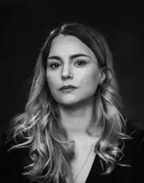 Close-up of a woman with long hair wearing a dark sweater and a necklace.