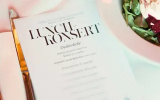 A plate of food is on a table together with a knife, fork and a concert program.