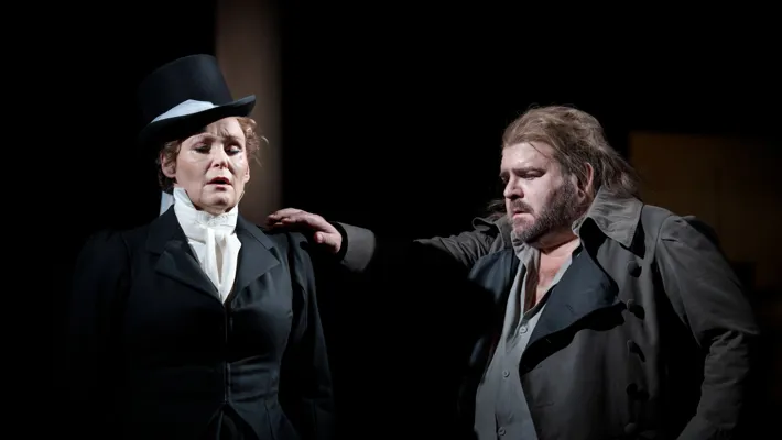 Woman with a top hat closes her eyes, a man reaches out his hand to touch her shoulder.