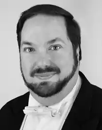 A close-up of a man with a beard wearing a tailcoat.