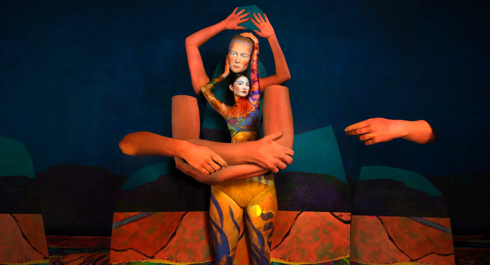 En kvinna håller en mask ovan sitt huvud, framför henne stora orangea rekvisita-armar.