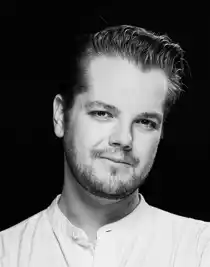 Close-up of a young man wearing a light, collarless shirt.
