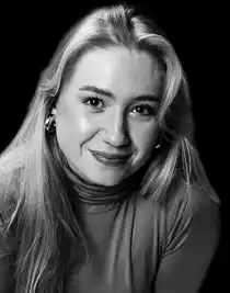 A woman with long blonde hair against a dark background.