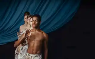 Fyra personer står i gåsarad mot ett mörkblått draperi, den första mannen håller en schackpjäs i handen.