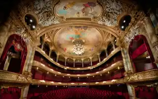 View of a large audience hall over several levels, red chairs and many gold decorations.